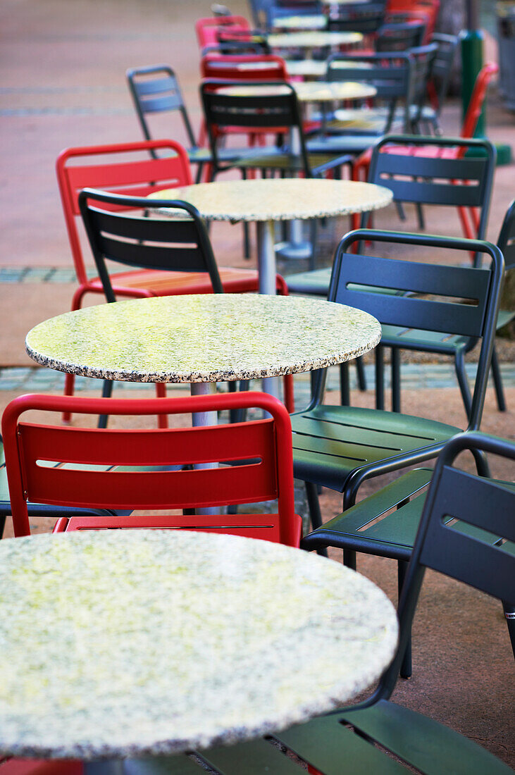 Mixture of red and grey chairs set out around round tables on sidewalk