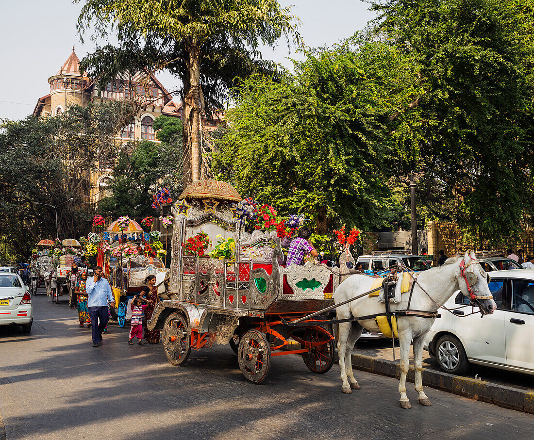 Row of decorated ornate horse drawn carriages parked on side of busy Mumbai street