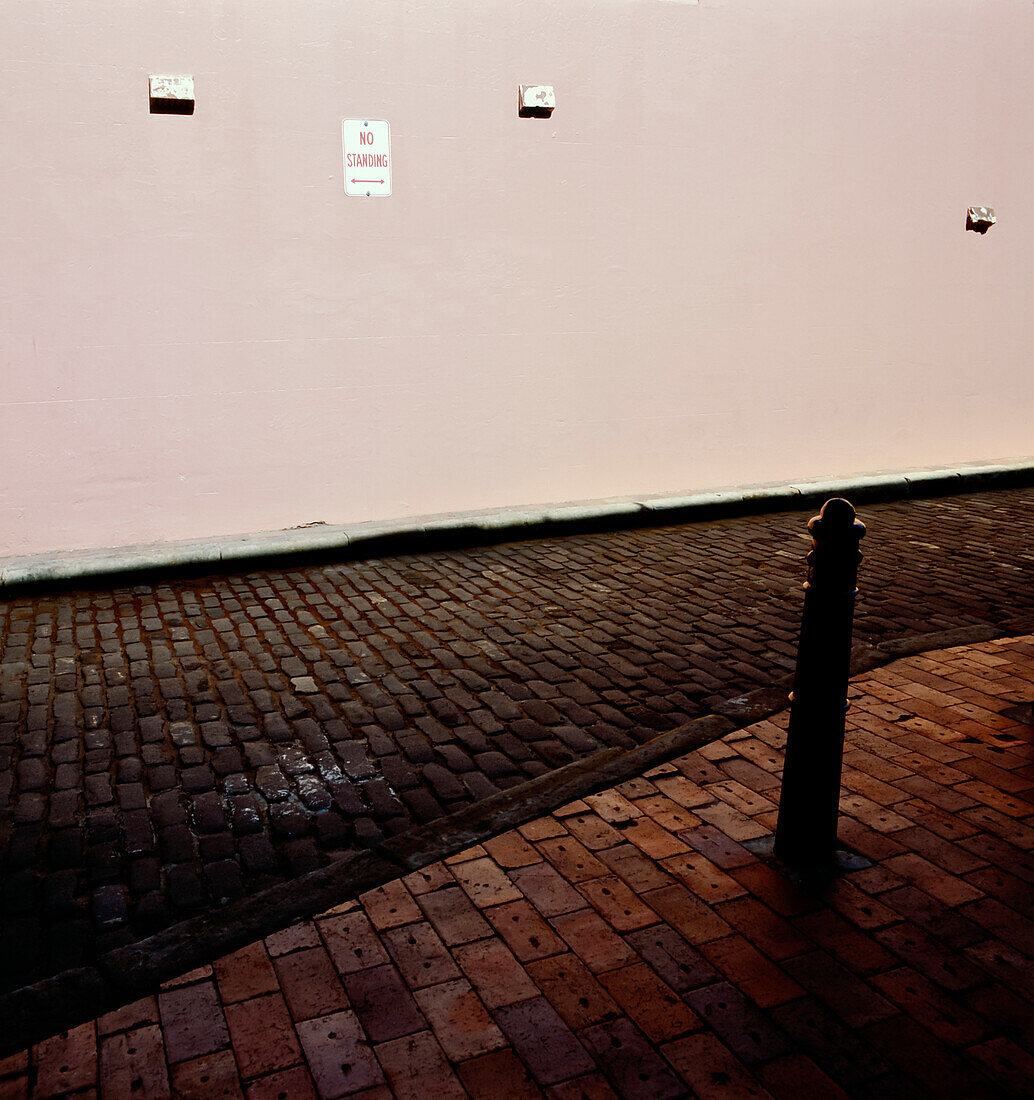 Kopfsteinpflasterstraße, die an die Betonwand des rosa gestrichenen Gebäudes angrenzt