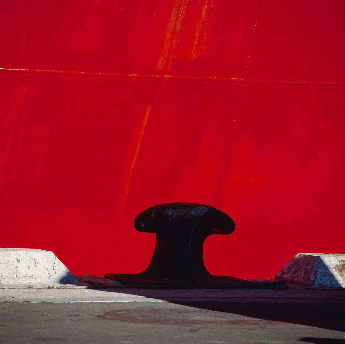 Close up of mooring bollard at wharf edge against hull of red ship