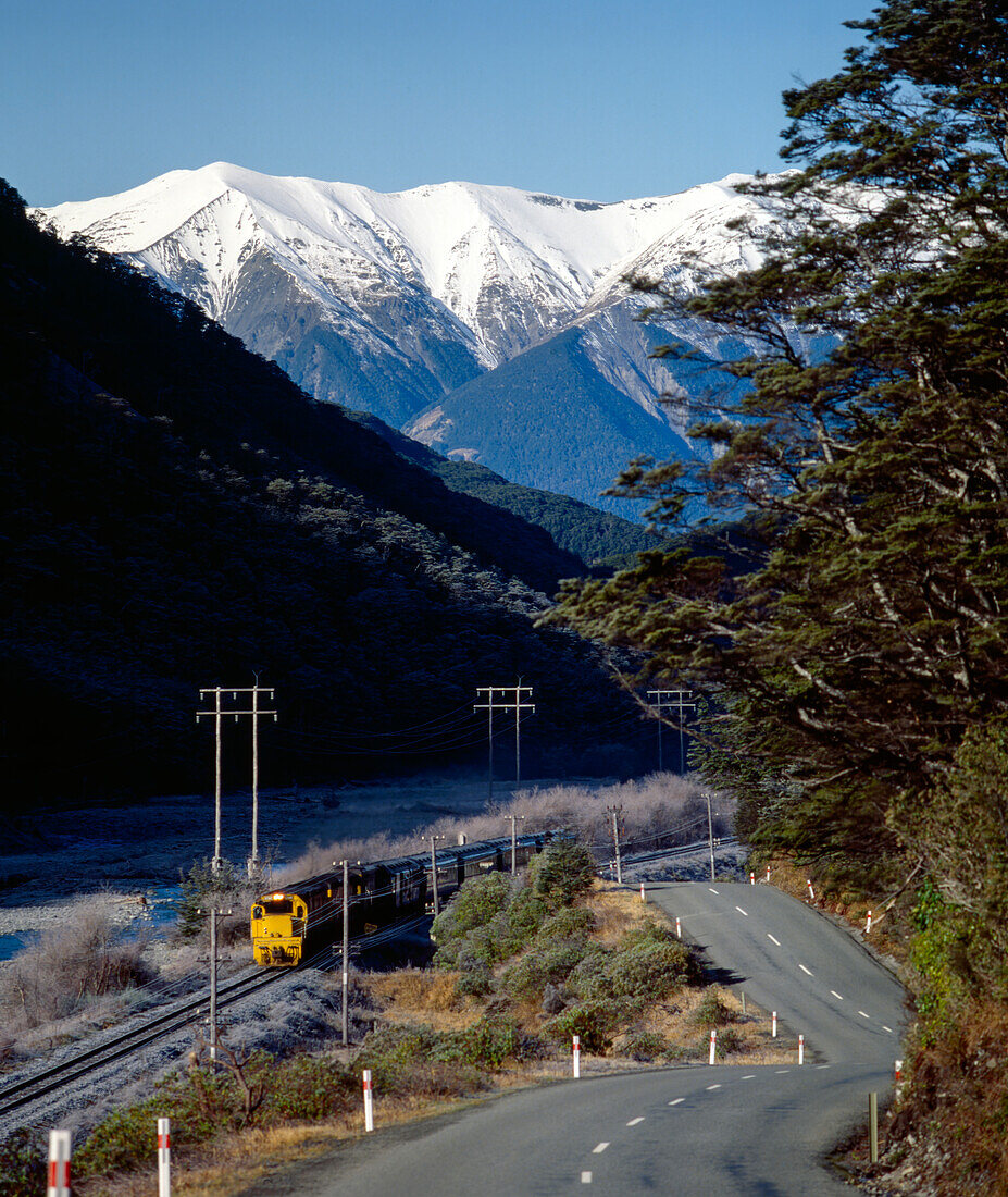 Zug unterwegs entlang Landstraße und schneebedeckte Berge im Hintergrund - Neuseeland