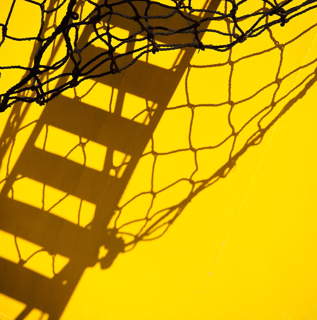 Shadow of gangplank against side of yellow ship and net hanging down