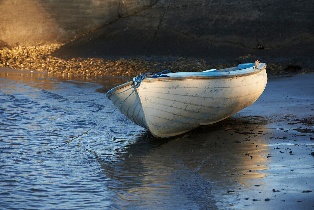 Dinghy tied at waters edge on sandy beach in front of rocky cliff