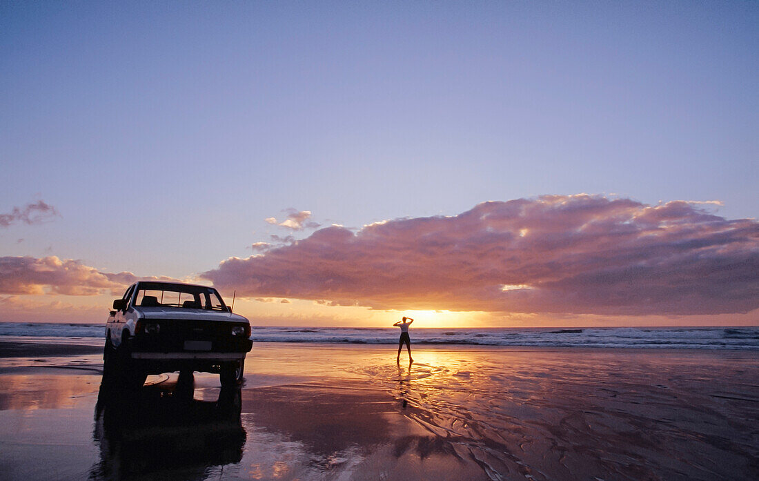 Weiße Ute parkte am Strand und einsame Person, die bei Sonnenuntergang am Wasser stand