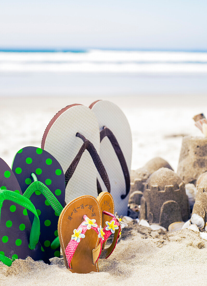 Hochkant im Sand stehende Flip Flops neben Sandburgen