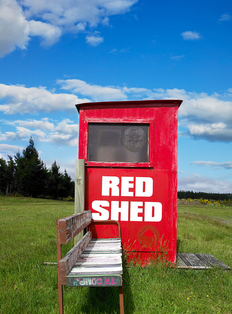 Old public phone box painted red and old seat in the middle of green field