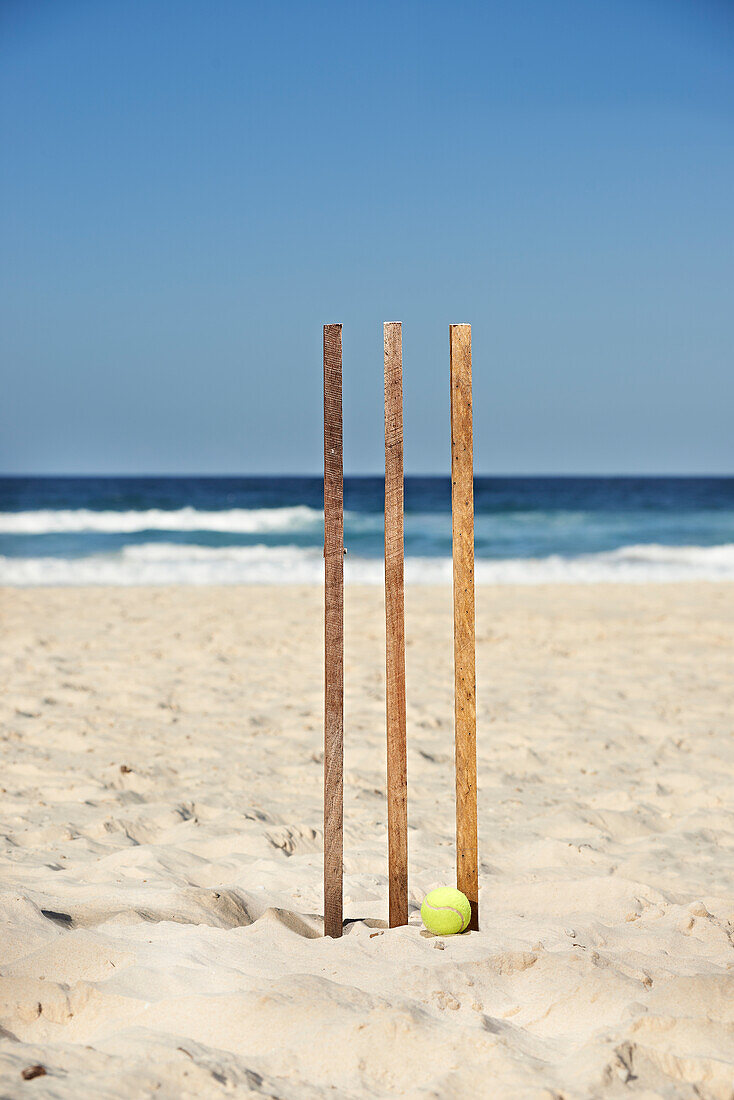 Cap with Australian flag resting on wooden cricket stumps and tennis ball at the beach
