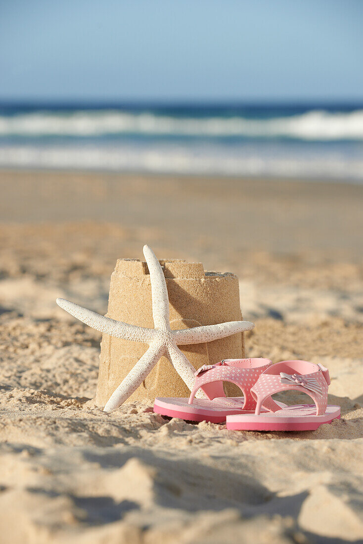 Flip flops and starfish next to sandcastle on the beach