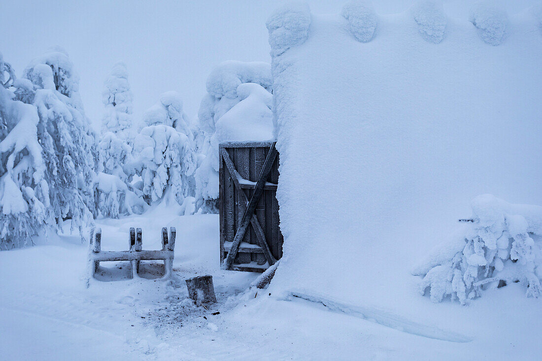 Blick auf einen schneebedeckten Holzschuppen nach einem Schneesturm in der Wildnis Finnisch-Lapplands, Winterszenerie