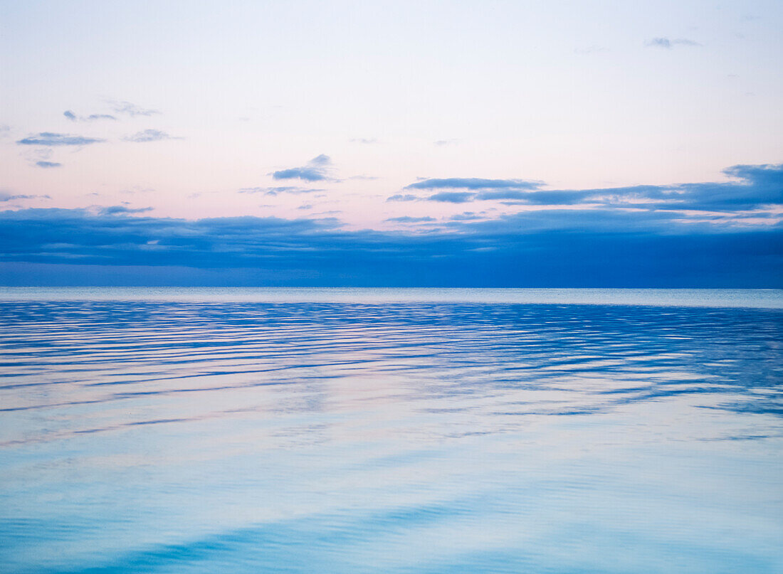 Sky meets sea on horizon line and clouds reflected in the calm rippling water