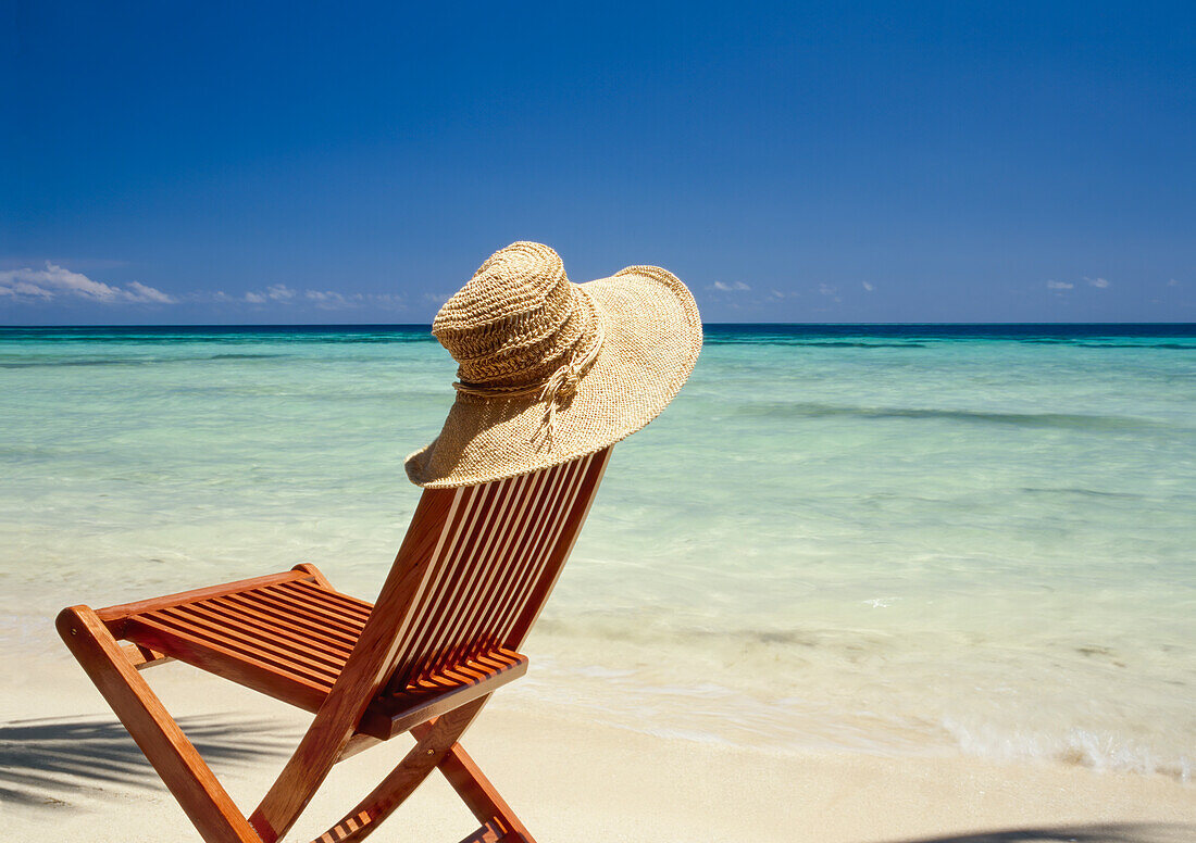 Sonnenhut ruht auf einem leeren Stuhl am tropischen Strand