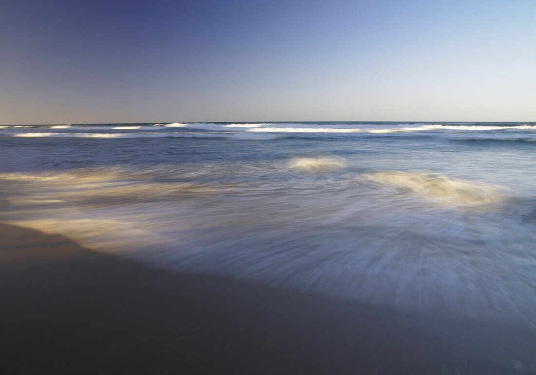 Wellen, die am späten Nachmittag sanft auf den Sand schlagen