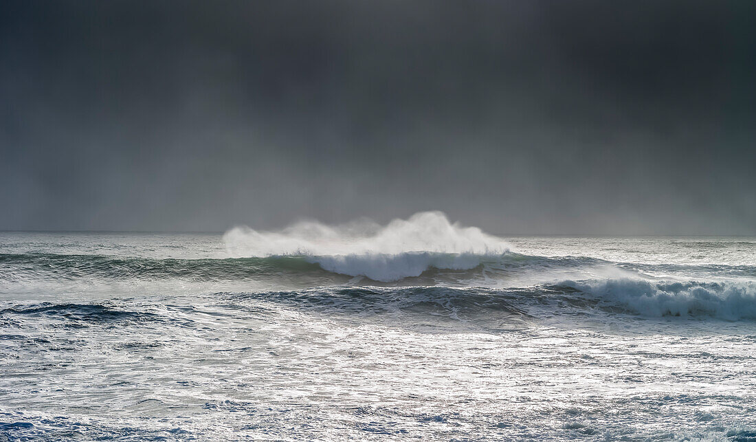 Welle kräuselt sich und bricht während des Zyklons Ola mit stürmischem Himmel