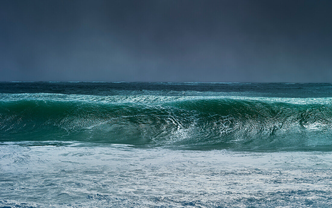 Huge wave curling over and breaking during cyclone Ola with stormy sky