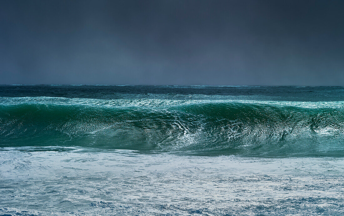Riesige Welle, die sich während des Zyklons Ola mit stürmischem Himmel kräuselt und bricht