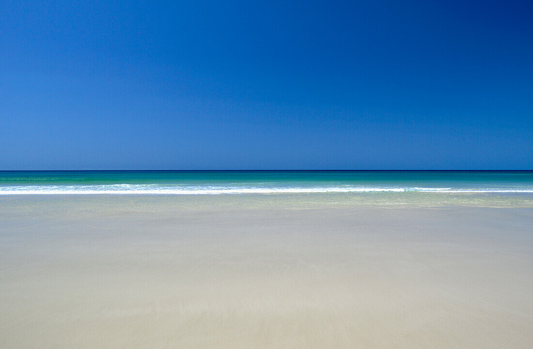 Calm tropical water meets blues sky and pristine sandy beach