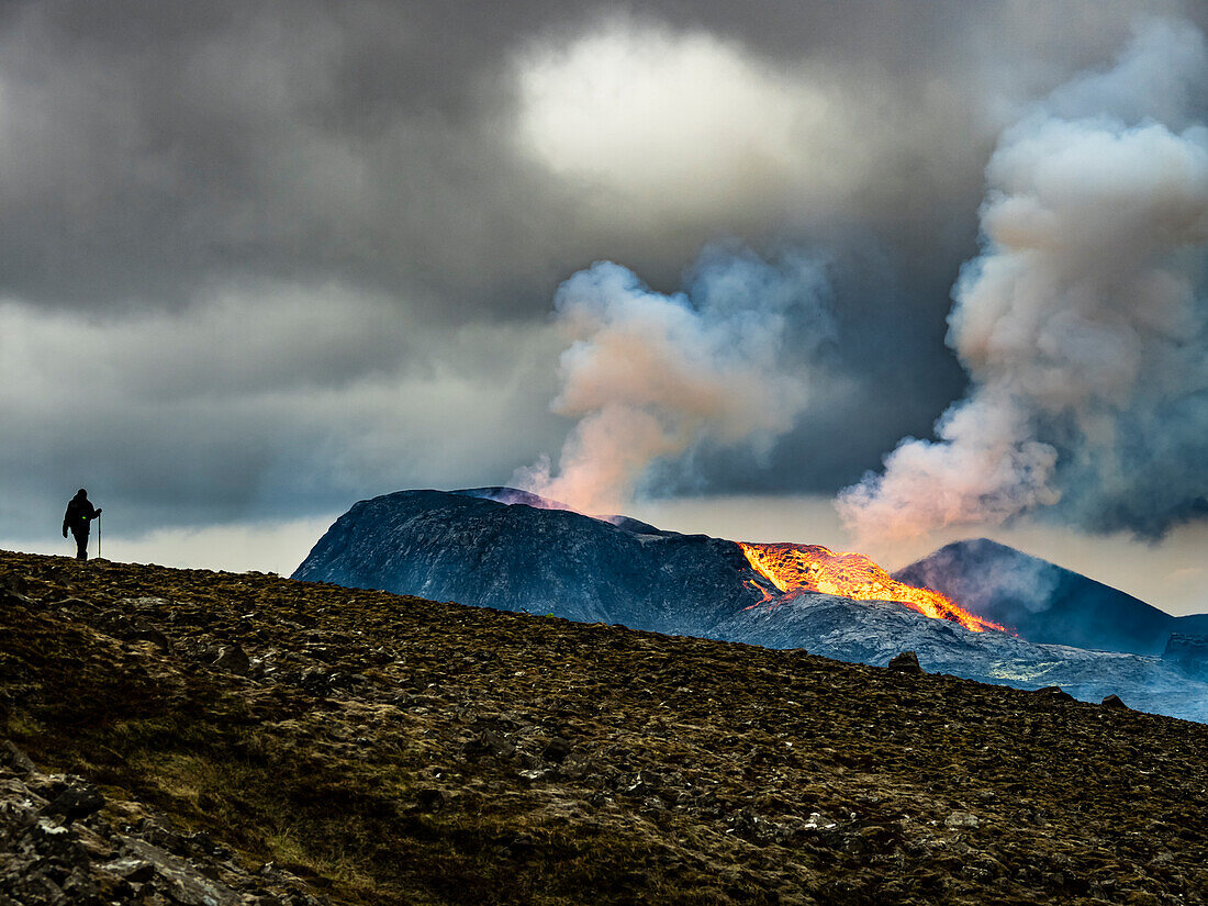 Einsamer Wanderer erklimmt den Observation Hill in Richtung glühender Lava und Dampfwolke vom Vulkan Fagradalsfjall, Island