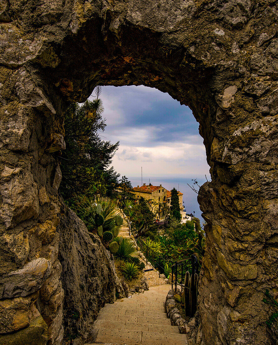 View through a stone arch in the Jardin Exotique of Èze on old houses of the village, Èze, French Riviera, France