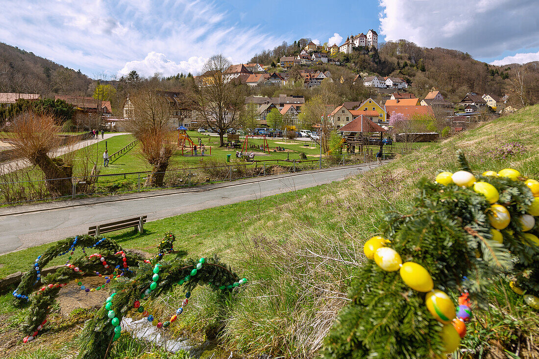 Easter fountain decorated with colorful Easter eggs, Brunnen am Gries in Egloffstein with a view of Egloffstein Castle in Franconian Switzerland, Bavaria, Germany