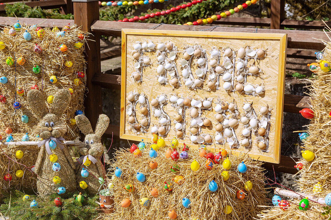 Frohe Ostern Tafel mit Eierschalen am der mit bunten Ostereiern geschmückte Osterquelle an der Trubachquelle in Obertrubach in der Fränkischen Schweiz, Bayern, Deutschland