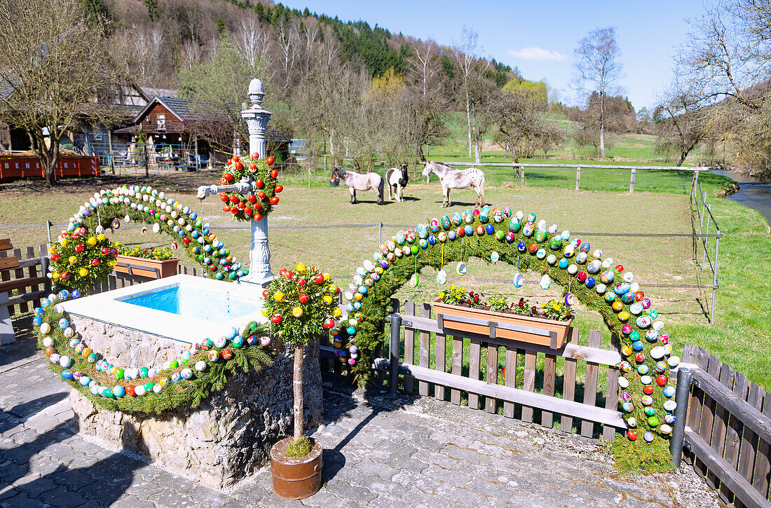 mit bunten Ostereiern geschmückter Osterbrunnen an der Leinleiter in Zoggendorf in der Fränkischen Schweiz, Bayern, Deutschland