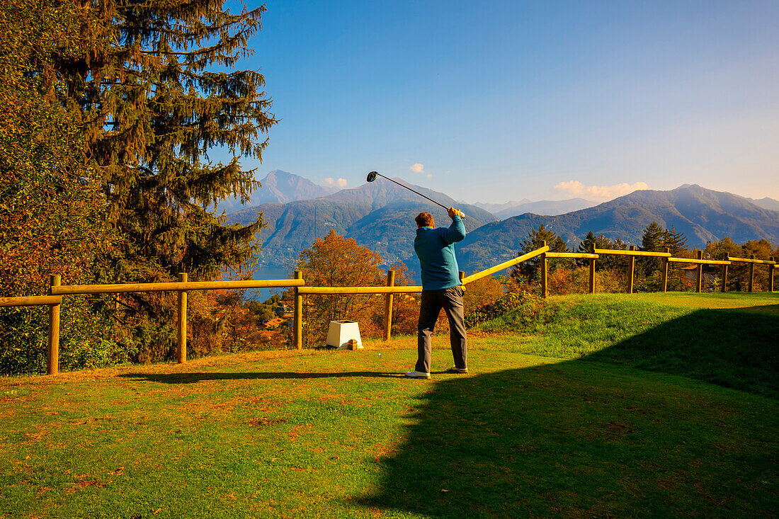Golfer Teeing Off with His Driver on Golf Course Menaggio with Mountain View in Autumn in Lombardy, Italy.