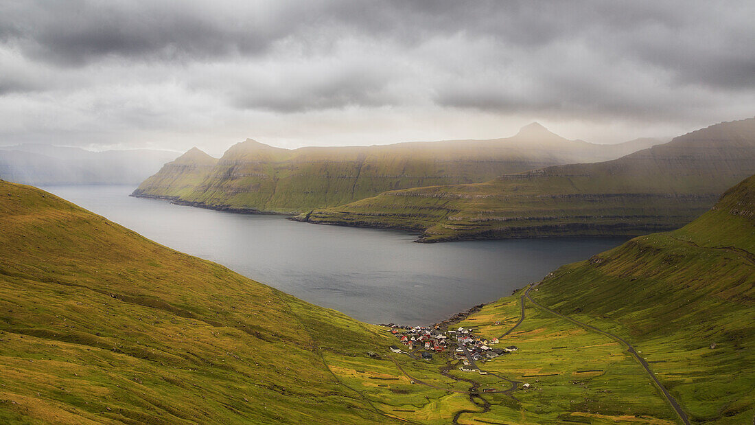 Blick auf einsames Dorf in weiter Landschaft. Funnings, Eysturoy, Färöer Inseln. Dunkle Wolken, Lichtschimmer