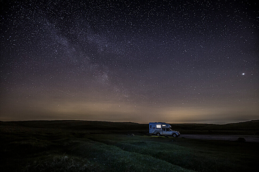 Lonely lit camper van, camper van at night under starry sky, milky way.