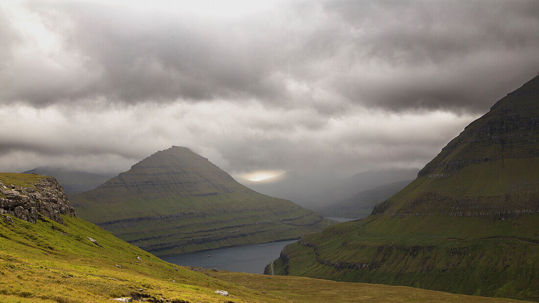 Funning Fjord, Eysturoy, Faeroere framed by green mountains. Dark clouds, cloud gap, sunshine