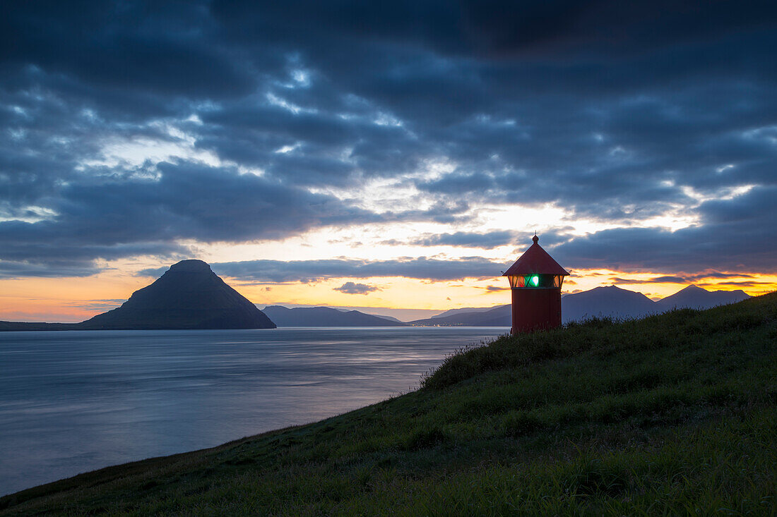 Kleiner roter Leuchtturm an grüner Küste. Berg im Meer. Velbastadur, Streymoy, Färöer.