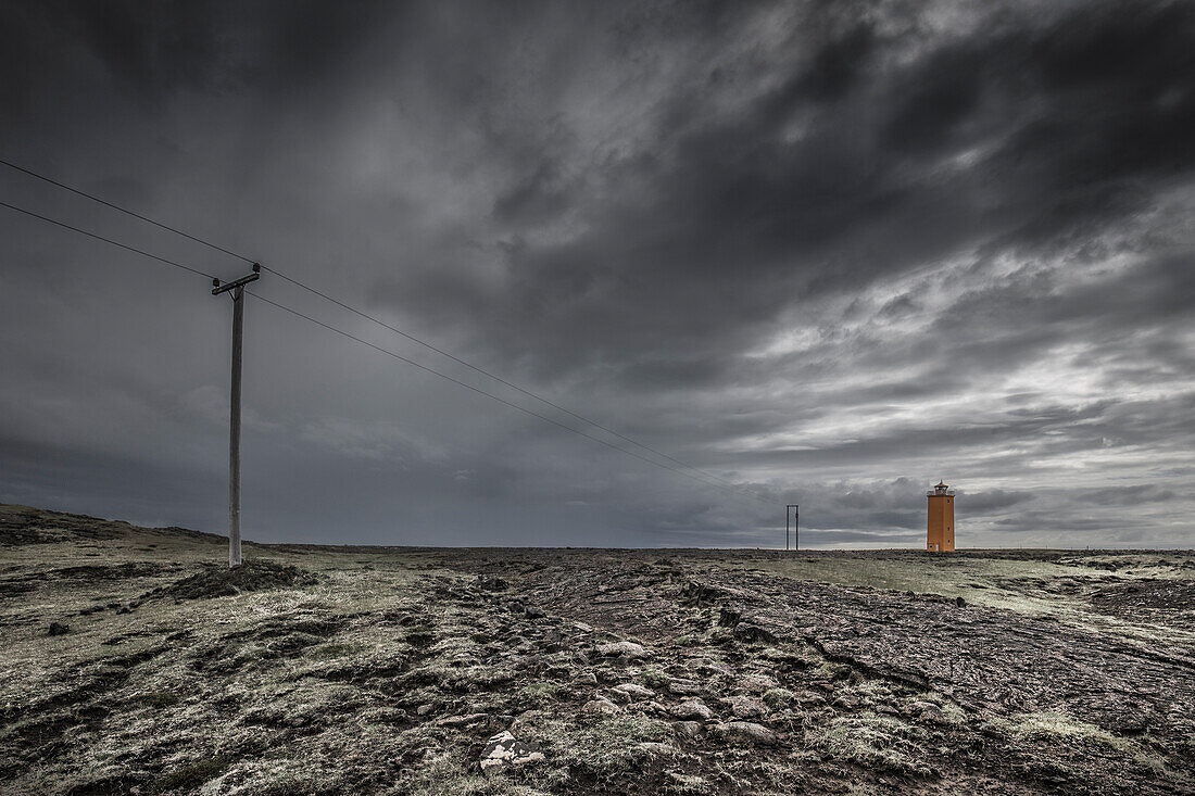 Slevogsviti lighthouse in rocky landscape. power lines. Dark sky. Olfus, Sudurland, Iceland.