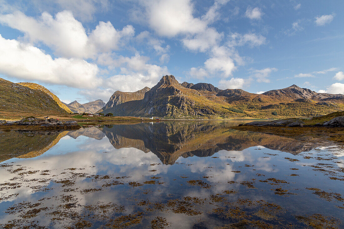 Mountains and sky are reflected in the fjord. Small house. Flakstad, Lofoten, Nordland, Norway