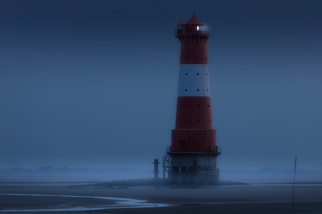 Arngast lighthouse at low tide in the Wadden Sea, Jade Bay, Lower Saxony, Germany. Illuminated.