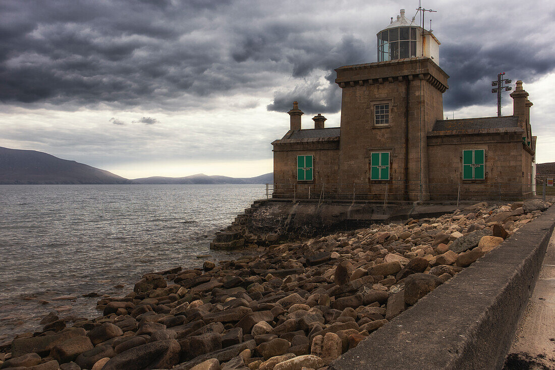 Blacksod lighthouse against dark rain clouds. quay wall. Fallmore, County Mayo, Ireland.