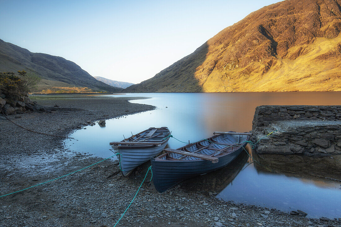 2 rowing boats are on the shore of the lake. Old stone jetty. mountains in the background. Sunrise. Doo Lough, Clashcame, Kilgeever, County Mayo, Ireland.