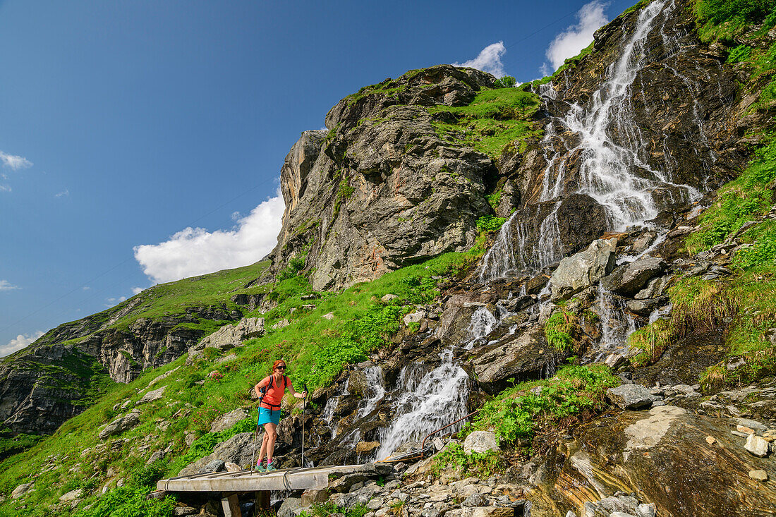 Mountaineering woman walking on bridge over waterfall, Floitental, Zillertal Alps Nature Park, Zillertal Alps, Tyrol, Austria