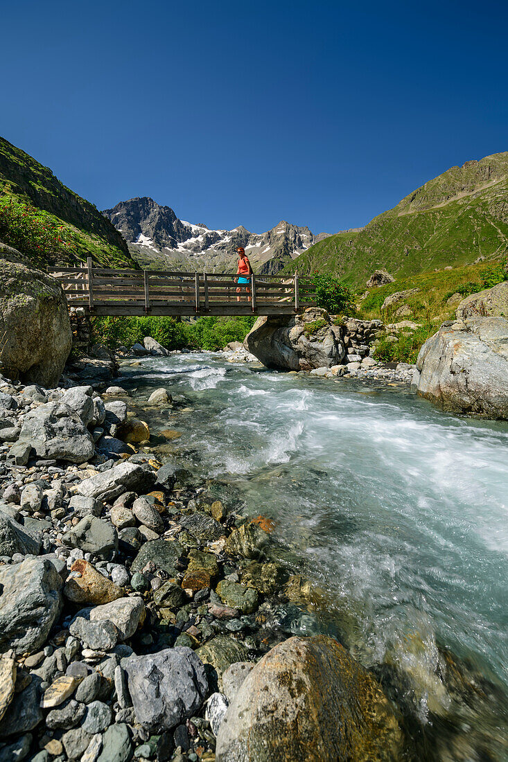 Frau beim Wandern geht auf Brücke über Bach Severaisse, Valgaudemar, Nationalpark Ecrins, Dauphine, Provence-Hautes Alpes, Frankreich