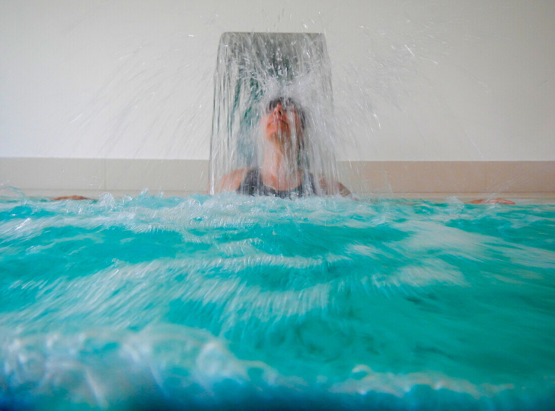 Frau im Massage-Pool mit fallendem Wasser im Schwimmbad in der Schweiz.