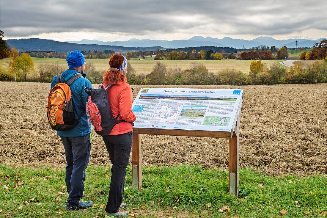 Man and woman hiking reading information board on the Holzkirchen Geology Trail, Holzkirchen geo-teaching trail, Upper Bavaria, Bavaria, Germany