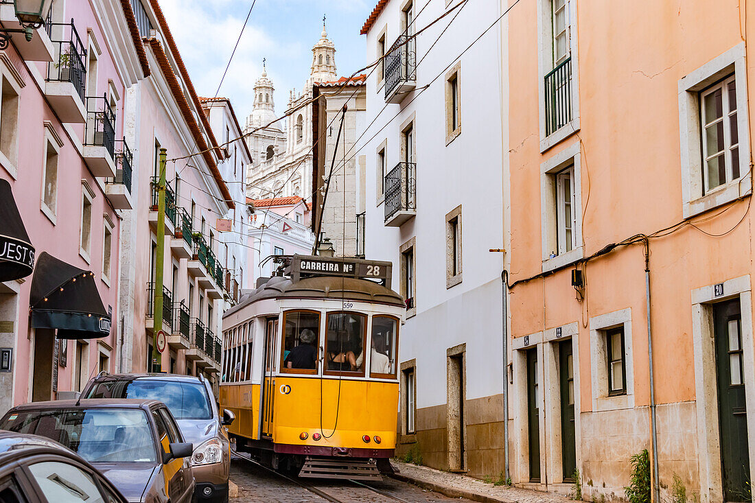 Die Straßenbahn der Linie 28E fährt durch eine steile und enge Straße in der Altstadt, Lissabon, Portugal