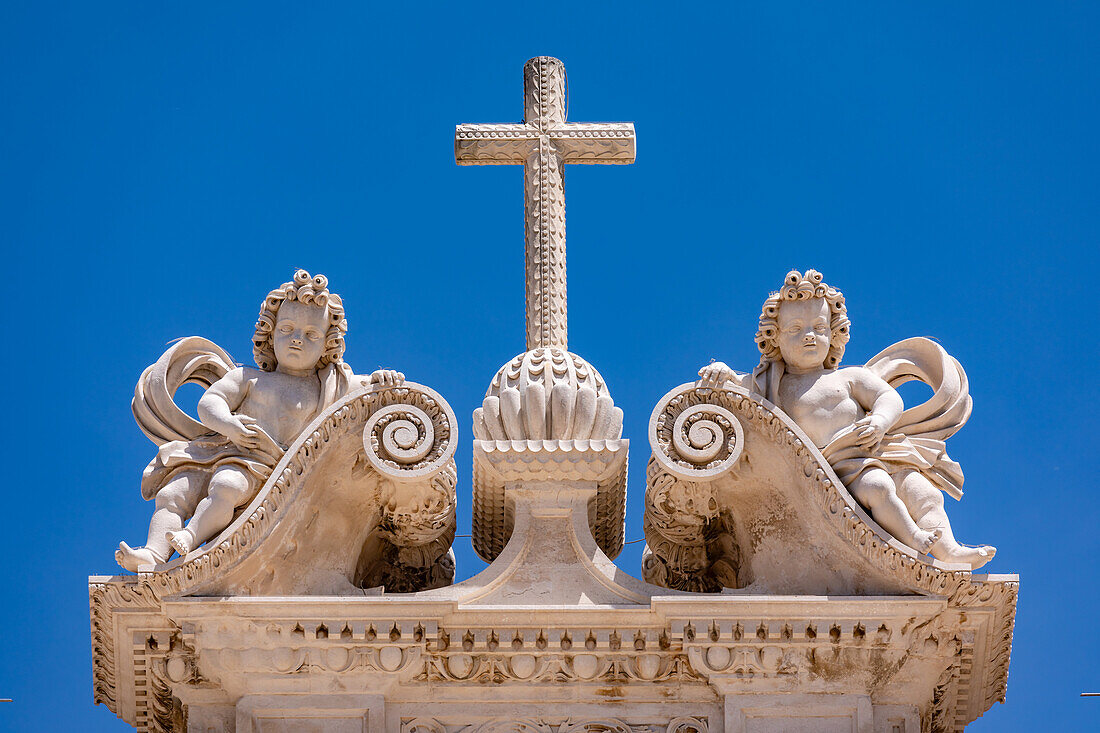 The cross with two angels at the top of the Royal Abbey of Alcobaca with a blue sky, Portugal