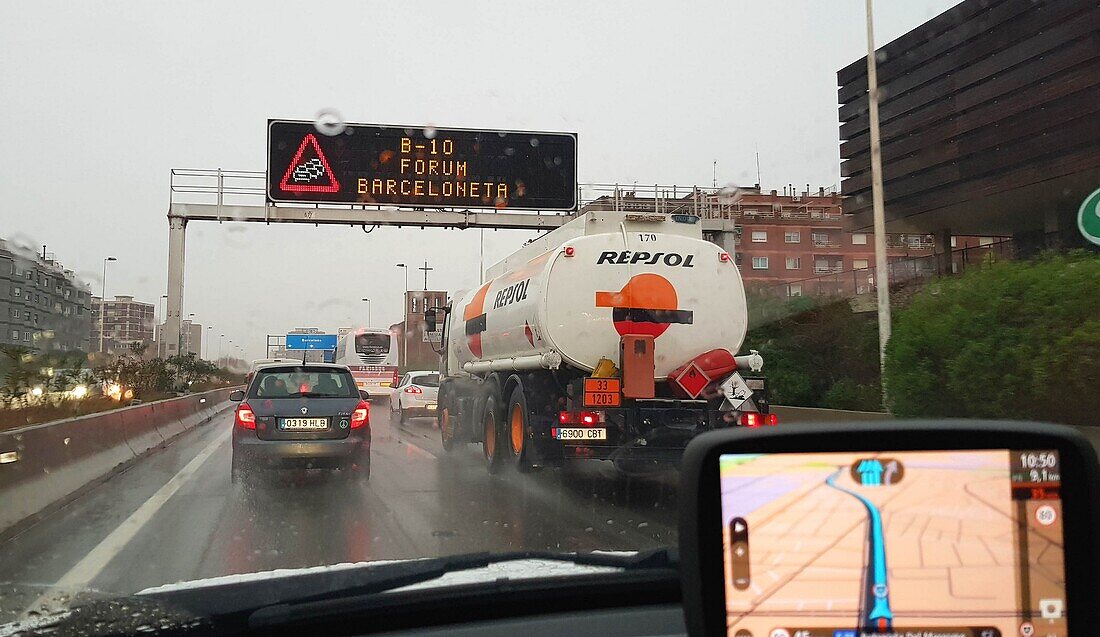 Autos und Lastwagen verkehren an einem regnerischen Tag auf der Autobahn in Richtung Barcelona. Das GPS zeigt die Route an. Barcelona. Katalonien. Spanien