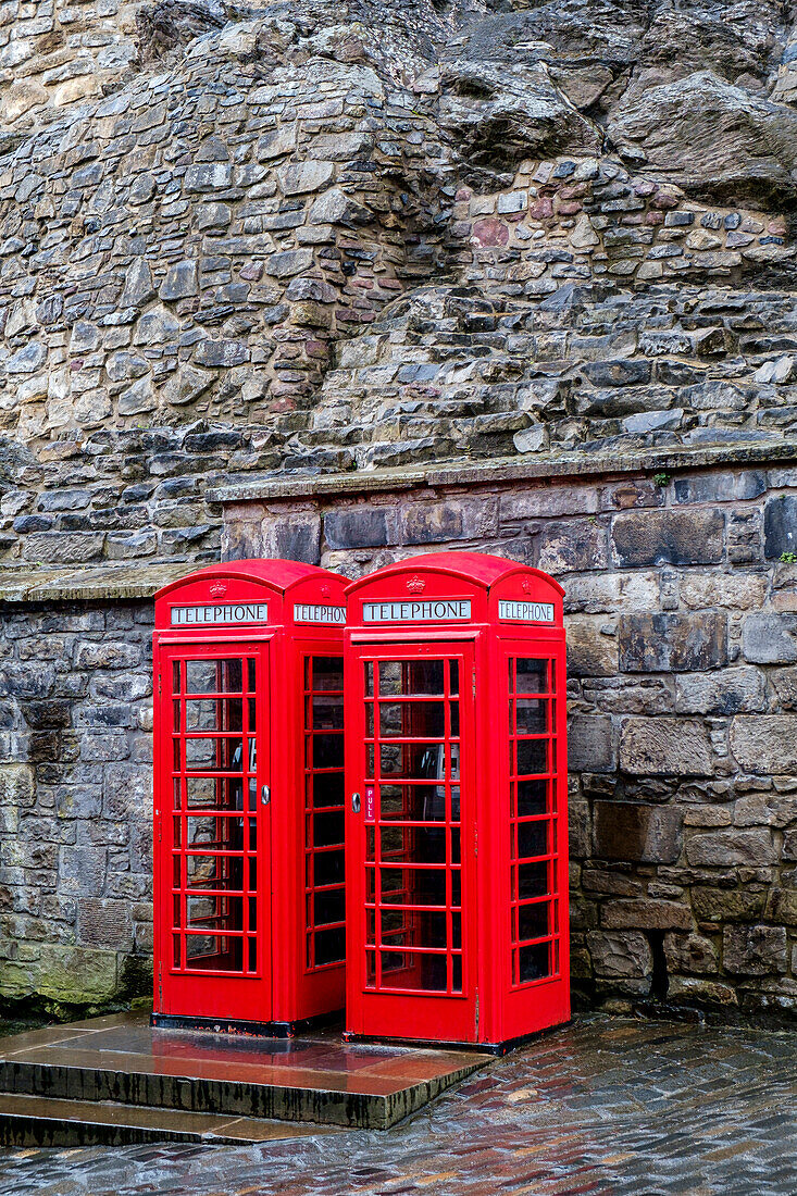 Red telephone boxes in front of ancient stone wall, Edinburgh, UK