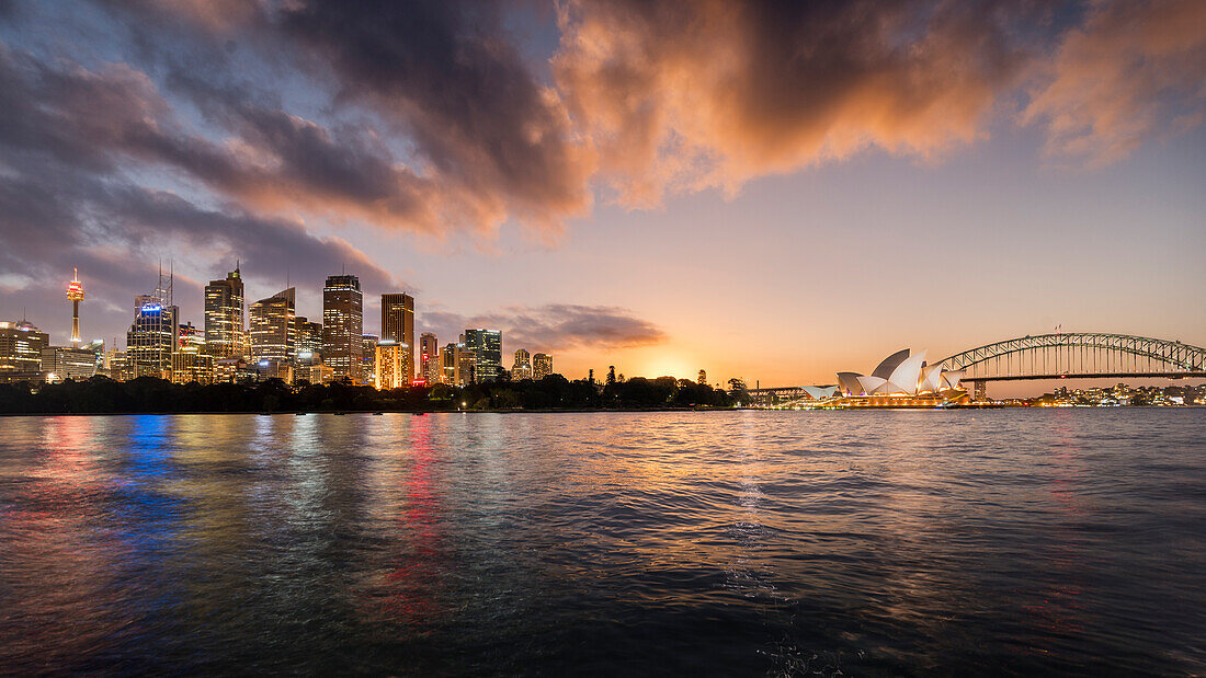 Sydney lit up at dawn seen from the water, including the Sydney Opera House.