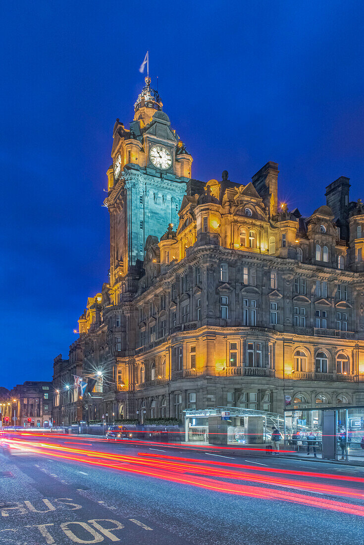 Clock tower of Balmoral Hotel lit up at night with traffic light blur below, Edinburgh, UK
