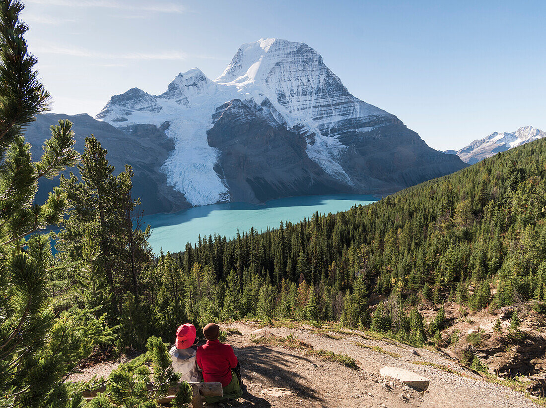 Two people resting by a hiking path, view of Mount Robson and the Rockies, Canada