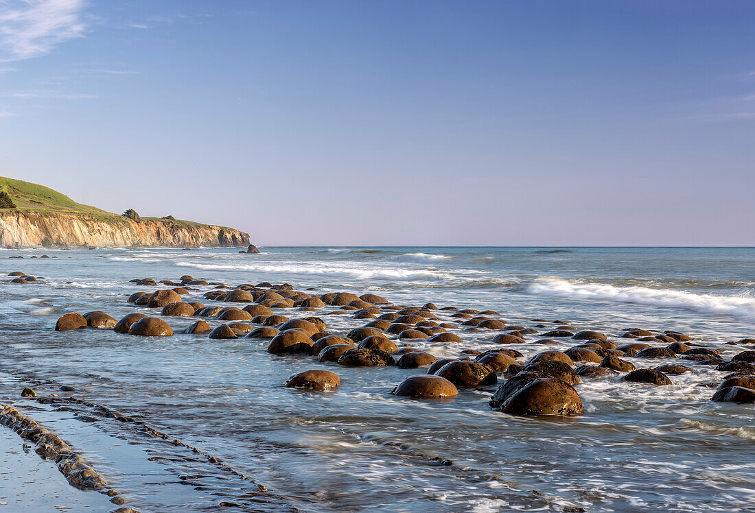 Rocks in shallow waves on Pacific Ocean at dusk.