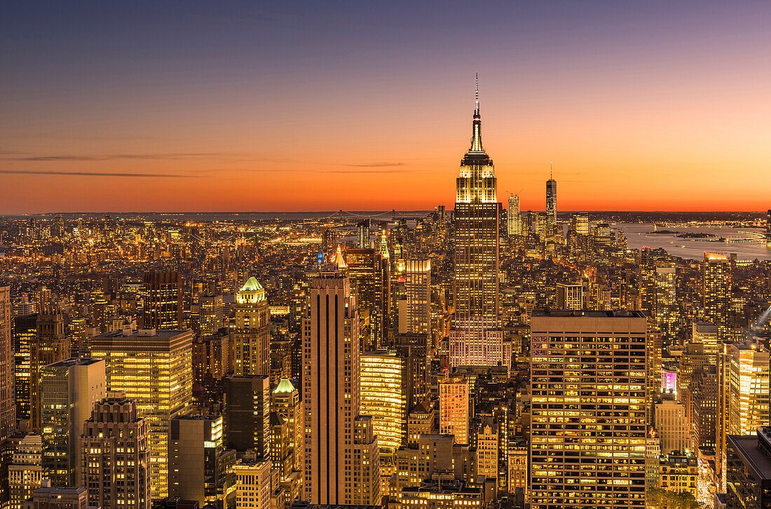 Empire state building rising above Manhattan skyline at sunrise or sunset.