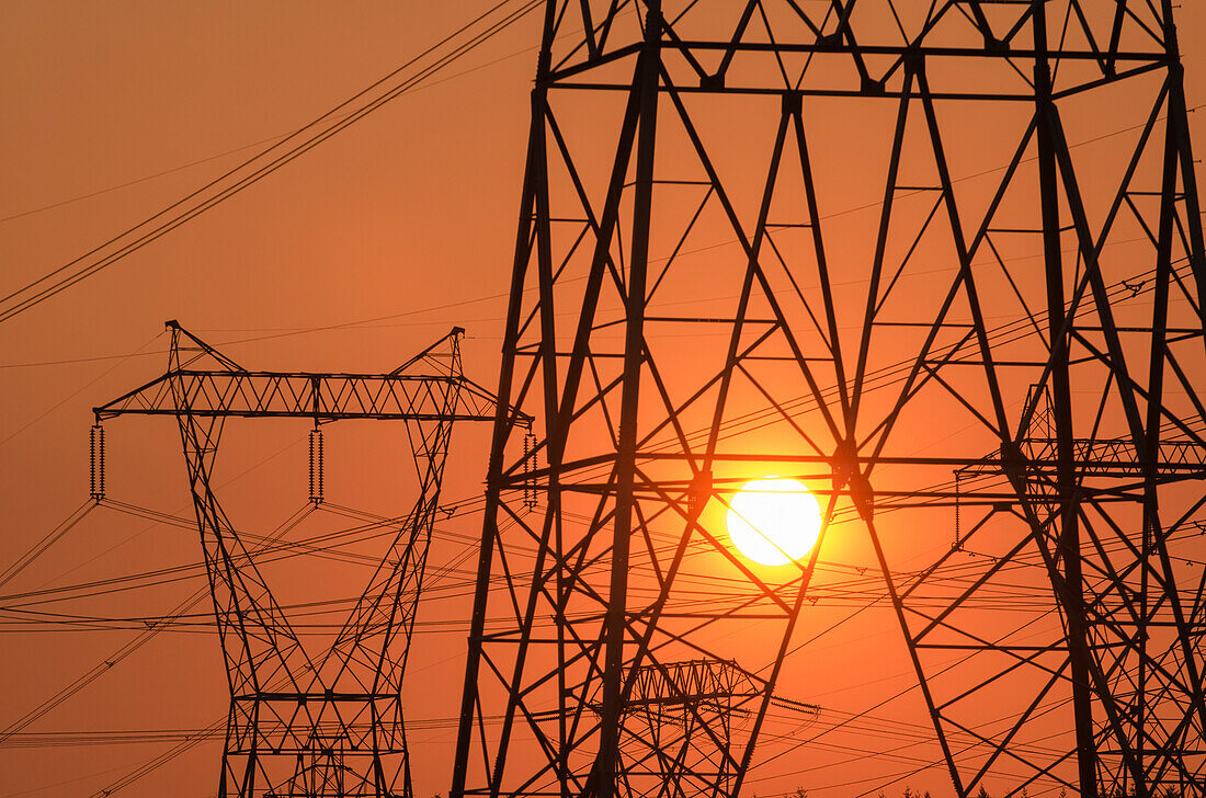 Electricity pylon and power lines with sun behind.