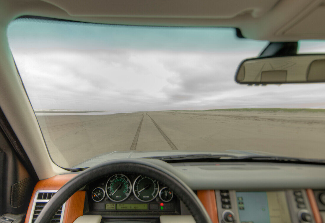 Beach and cliffs seen from driver's seat of a car, with steering wheel in foreground.